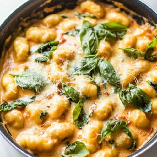 Creamy Tuscan gnocchi in a skillet with sun-dried tomatoes, spinach, and parmesan cream sauce