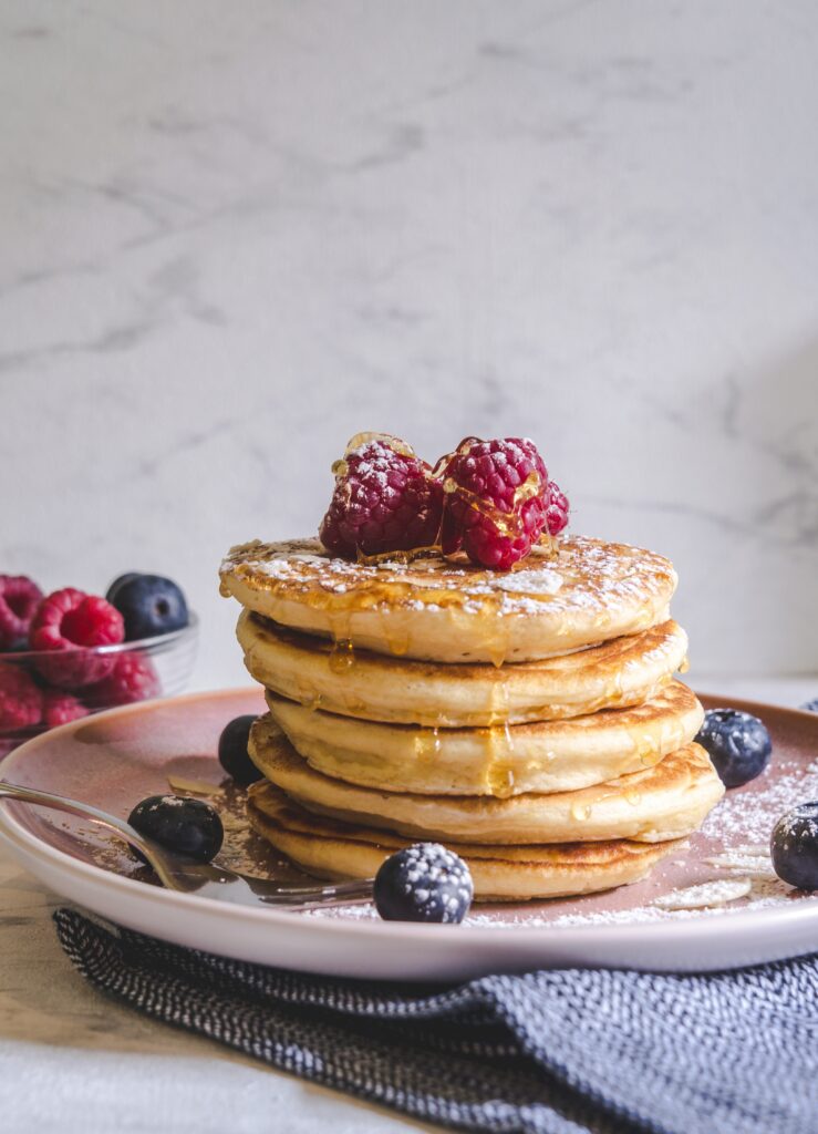 Stack of fluffy homemade pancakes drizzled with maple syrup and topped with fresh berries and butter