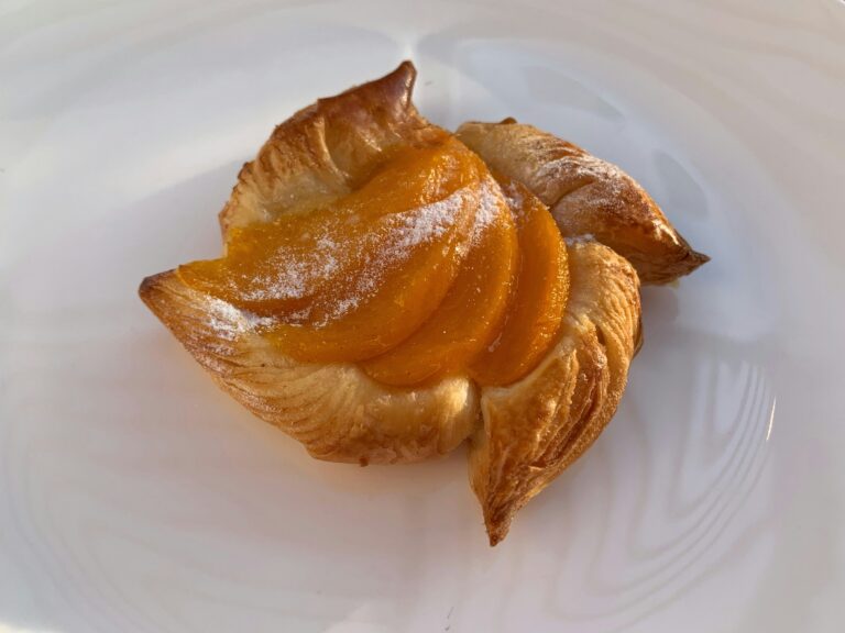 Easy peach puff pastry tart with golden flaky crust, fanned peach slices and powdered sugar on white plate