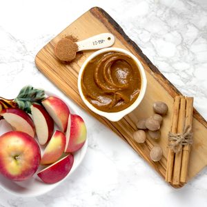Easy caramel apple dip in a white bowl on a wooden board with fresh sliced apples cinnamon sticks and warm spices on a marble background